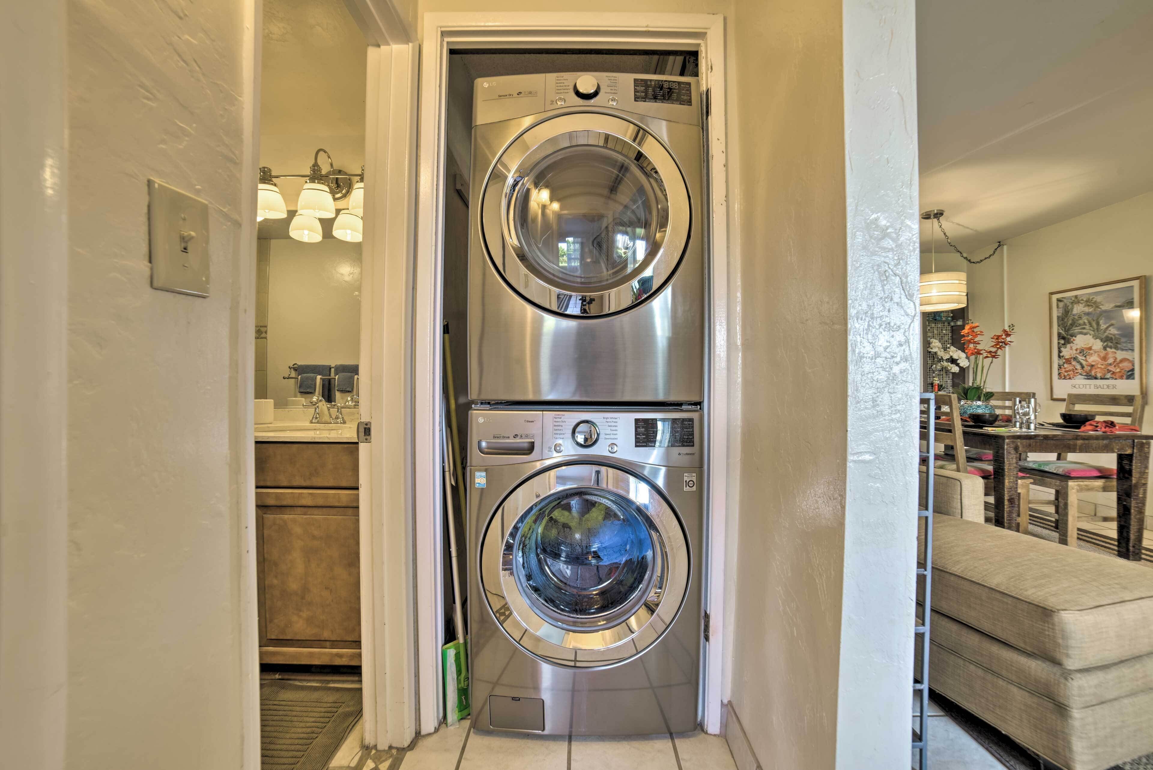 A compact laundry room with two stainless steel front-loading washing machines, a small sink, and a light fixture above the machines.