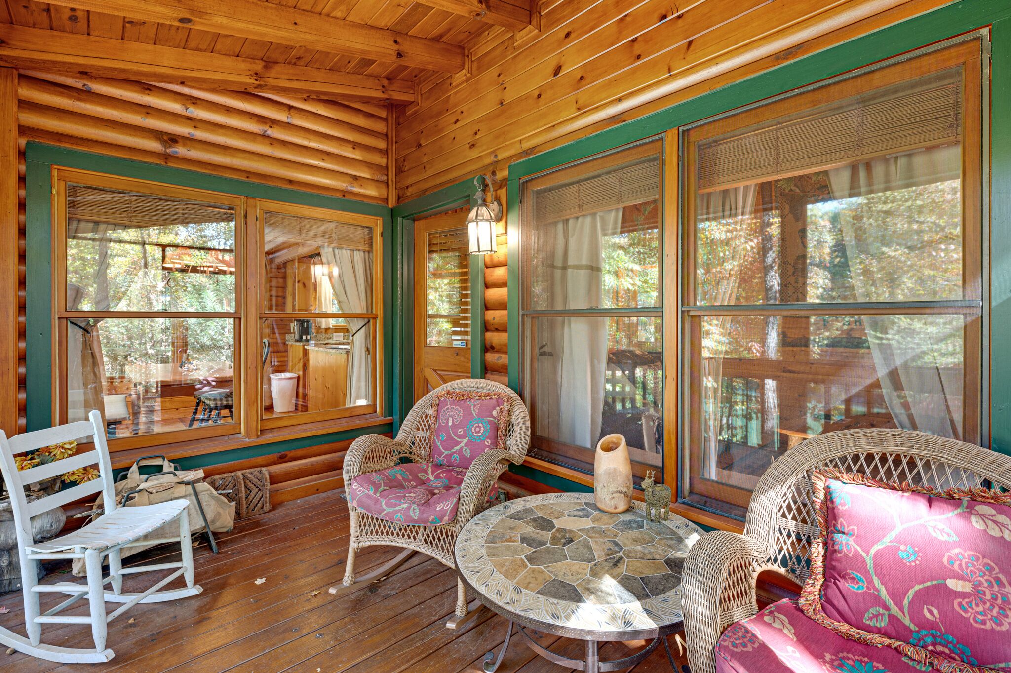A wooden cabin interior with wicker furniture, large windows, and a stone-tiled table.