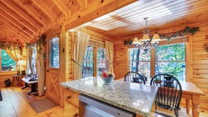 Interior de una cabaña de madera con zona de cocina, encimera de granito, lavavajillas y mesa de comedor con sillas.