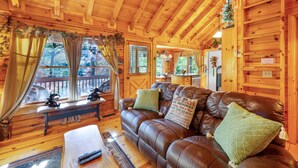 Interior acogedor de una cabaña con sofá de cuero, paredes de madera y ventana con vista a una terraza.