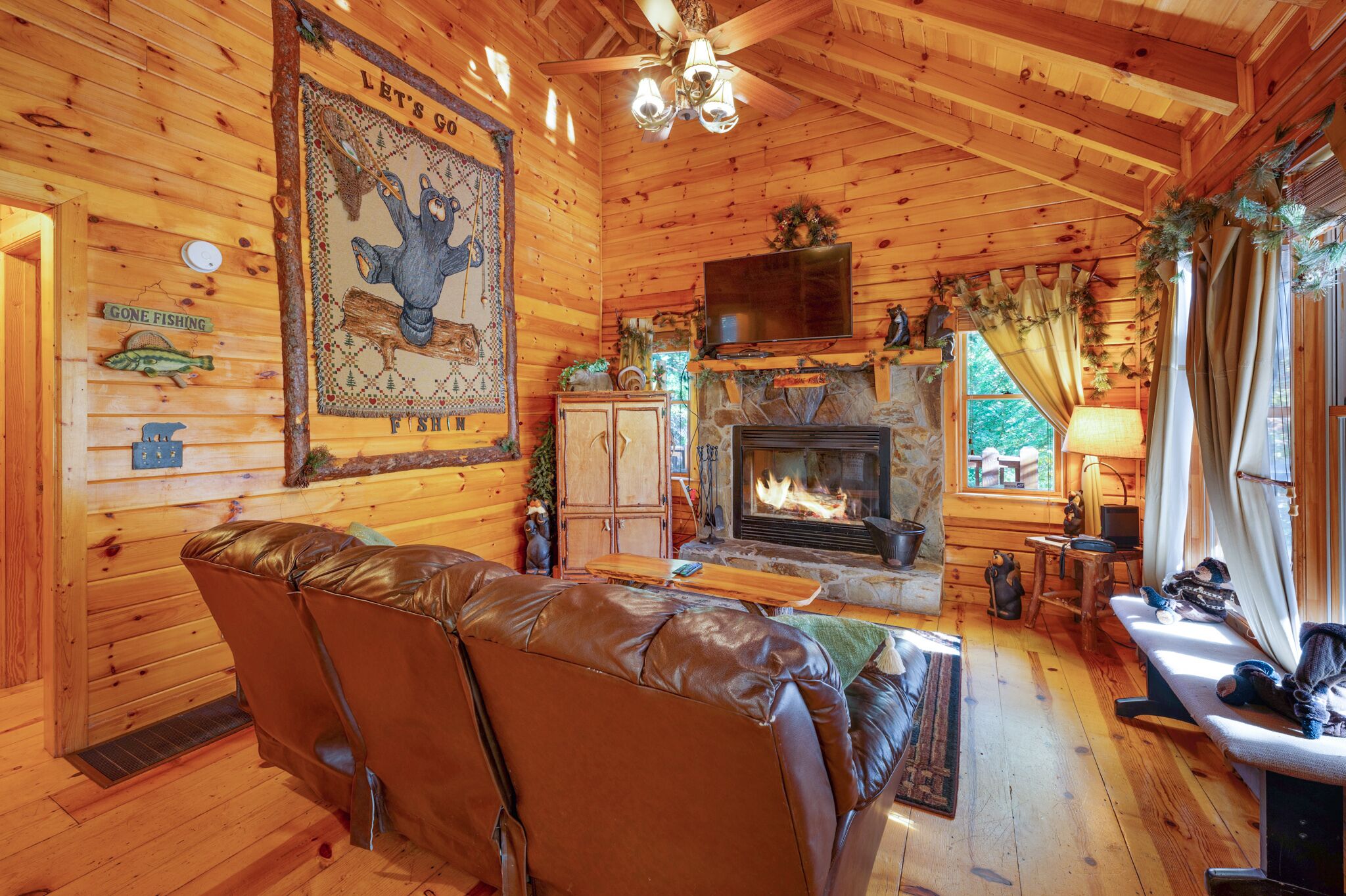 A cozy cabin interior with a fireplace, leather sofa, wooden walls, and a television.