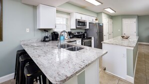 Una cocina moderna con gabinetes blancos, encimera de granito y electrodomésticos de acero inoxidable.