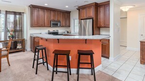 A kitchen with wooden cabinets, a stainless steel refrigerator, a granite countertop, and a bar stool. - Beautiful and spacious townhouse located on the boardwalk with a pool! (OCEAN CITY)