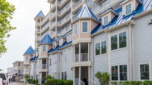 A row of multi-story buildings with balconies, a street in front, and a parked car. - Beautiful and spacious townhouse located on the boardwalk with a pool! (OCEAN CITY)