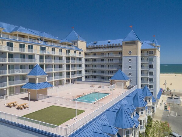 A multi-story hotel with a pool area, multiple balconies, and a beach view.