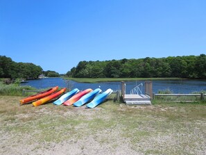 A dock with canoes lined up on the grass beside a calm river. - Harwich Port Retreat—Walk to Beach & Rail Trail (Harwich Port)