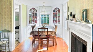 A dining room with a wooden table and chairs, a fireplace, and a view through arched windows.