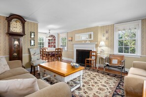 A traditional living room with a fireplace, a dining area with wooden furniture, and a large wall clock.