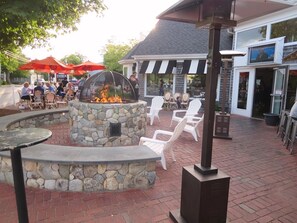 An outdoor patio with a stone fire pit, white chairs, and tables.