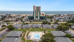 A hotel with a central building, a swimming pool, and a view of the ocean.