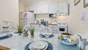 A compact kitchen with white cabinets, a microwave, and a stove. There are decorative plants on the counter and a bag of groceries.
