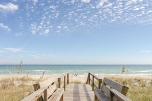 A wooden boardwalk leading to a beach with a clear sky.