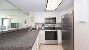 A modern kitchen with white cabinets, stainless steel appliances, a granite countertop, and a large window. - Comfortable, cozy 3-bedroom oceanfront condo with free WiFi, a breathtaking ocean view, an indoor and outdoor pool, and more located uptown and mere steps to the beach! (Ocean City)