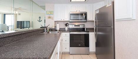A modern kitchen with white cabinets, stainless steel appliances, a granite countertop, and a large window.
