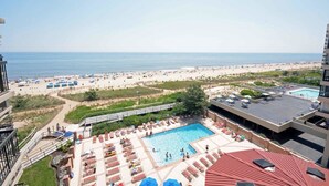 A rooftop pool area with a view of the beach and ocean. - Comfortable, cozy 3-bedroom oceanfront condo with free WiFi, a breathtaking ocean view, an indoor and outdoor pool, and more located uptown and mere steps to the beach! (Ocean City)