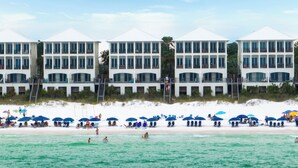 A beachfront hotel with multiple balconies, a sandy beach, and several umbrellas.