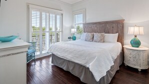 A bedroom with a large bed, a nightstand with a lamp, a dresser, and a window with blinds.