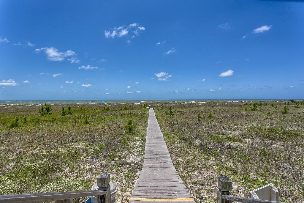 A wooden boardwalk leading to a beach with a clear sky.