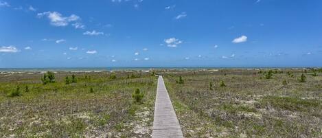 A wooden boardwalk leading to a beach with a clear sky.