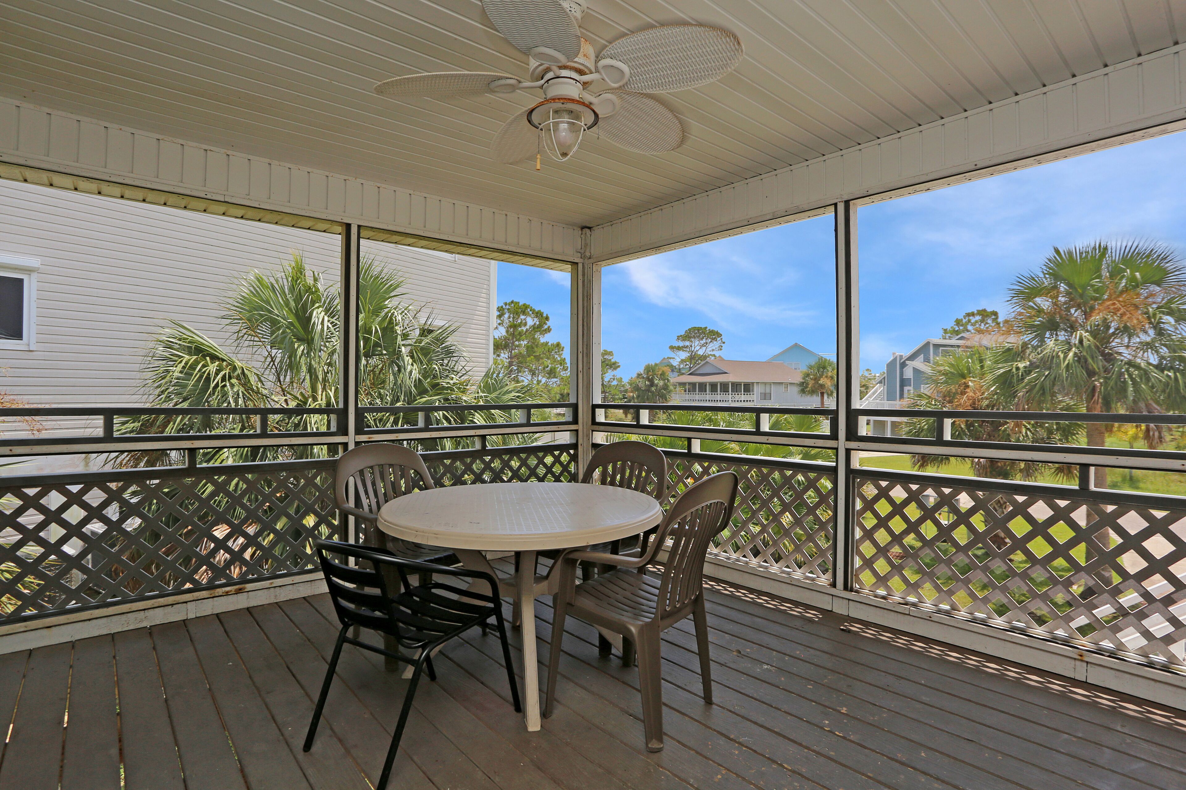 A covered outdoor area with a table and chairs, a ceiling fan, and a view of houses and trees.
