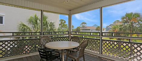 A covered outdoor area with a table and chairs, a ceiling fan, and a view of houses and trees.