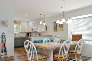 A dining area with a wooden table, white chairs, and a kitchen in the background.