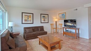 Een woonkamer met een bruine bank, twee abstracte schilderijen in lijsten, een houten salontafel, een tv op een houten dressoir, en een lamp.