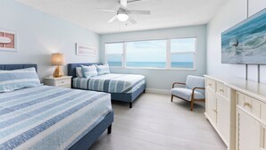 A bedroom with two beds, a ceiling fan, a large window, a TV, and a view of the ocean. - Direct Oceanfront Condo with Heated Pool, BBQ Grills, Private Balcony & Beach Access! 🌴 (Satellite Beach)