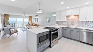 A modern kitchen with a central island, stainless steel appliances, and a view to the outside. - Direct Oceanfront Condo with Heated Pool, BBQ Grills, Private Balcony & Beach Access! 🌴 (Satellite Beach)