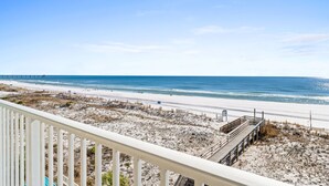 Une vue sur la plage depuis un balcon avec une terrasse en bois, une plage de sable et l’océan.