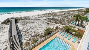 Vue sur la plage depuis le balcon d’un hôtel, avec une piscine et des chaises longues.