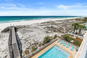 A beach view from a hotel balcony with a pool and lounge chairs.