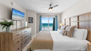 Une chambre à coucher avec un lit, une commode, une télévision, un ventilateur de plafond et une vue sur l’océan.
