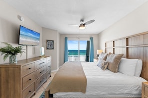 A bedroom with a bed, dresser, TV, ceiling fan, and a view of the ocean.