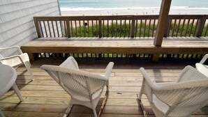 Una terraza de madera con sillas de mimbre con vista a la playa.