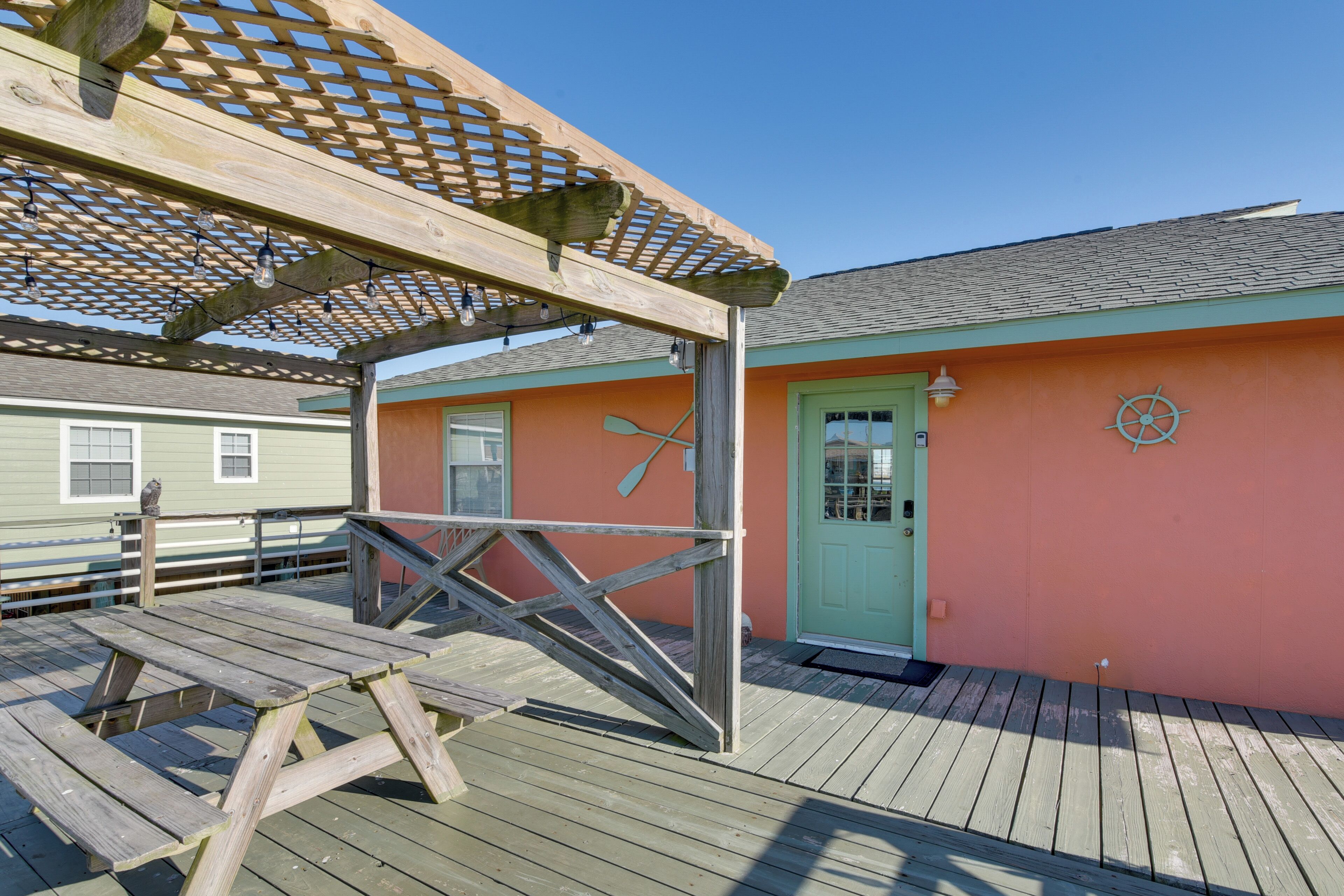 A wooden deck with a pergola overhead, a green door, and a wheel symbol on the wall.