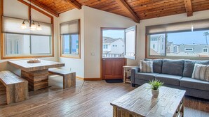 A cozy living room with a wooden ceiling, a gray sofa, a wooden coffee table, and a view of the neighborhood through large windows.