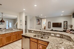 A modern kitchen with granite countertops, wooden cabinets, a stainless steel sink, and a built-in dishwasher. - Sunset Home with Modern Living at Encore (Kissimmee)