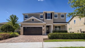 A two-story residential house with a garage, a brick driveway, and well-maintained landscaping. - Sunset Home with Modern Living at Encore (Kissimmee)