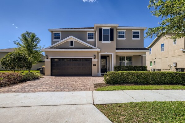 A two-story residential house with a garage, a brick driveway, and well-maintained landscaping. - Sunset Home with Modern Living at Encore (Kissimmee)