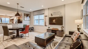 A modern living room with a sofa, coffee table, and dining area. - Sunset Home with Modern Living at Encore (Kissimmee)