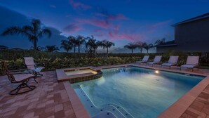 A swimming pool with lounge chairs, a hot tub, and a view of palm trees at dusk. - Sunset Home with Modern Living at Encore (Kissimmee)