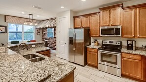 A modern kitchen with granite countertops, stainless steel appliances, and wooden cabinets. - Sunset Home with Modern Living at Encore (Kissimmee)