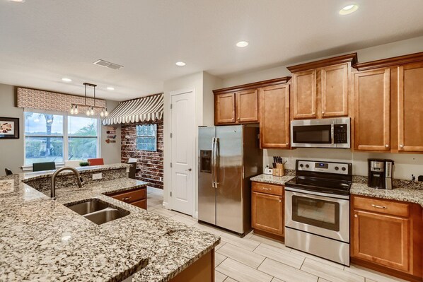 A modern kitchen with granite countertops, stainless steel appliances, and wooden cabinets. - Sunset Home with Modern Living at Encore (Kissimmee)