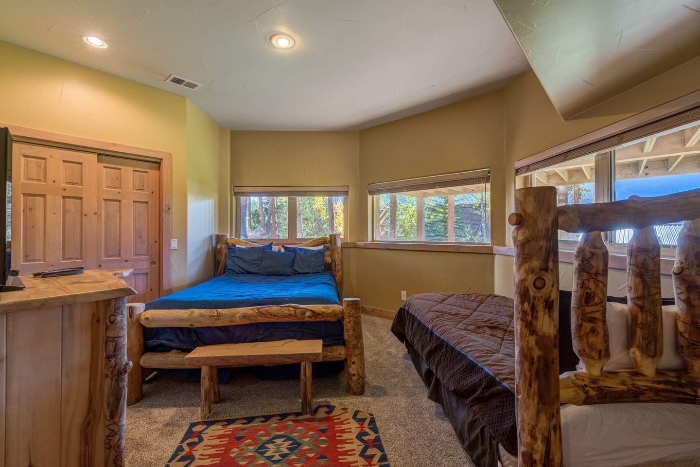 A bedroom with a wooden bed frame, a desk, and a window with a view of trees.