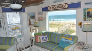Ein wohnzimmer im Strandhausstil mit Meerblick, einem gestreiften Sofa und einem Schild mit der Aufschrift "BEACH HOUSE".
