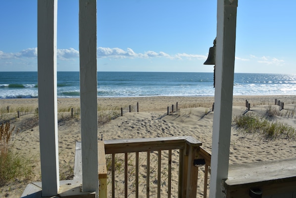 A beach view from a wooden deck with a railing, sandy beach, and ocean waves.