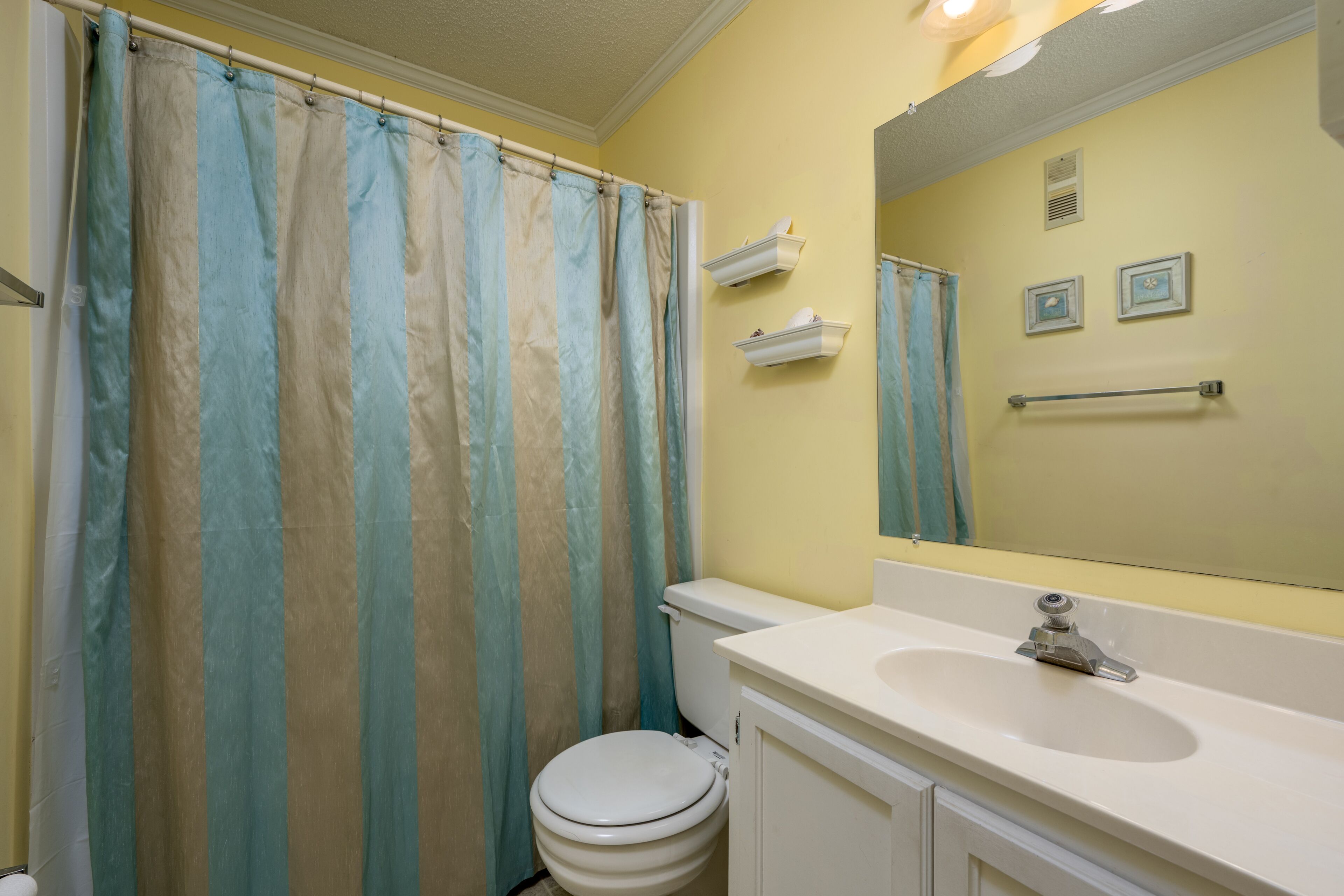 A bathroom with a shower curtain, toilet, sink, and mirror.