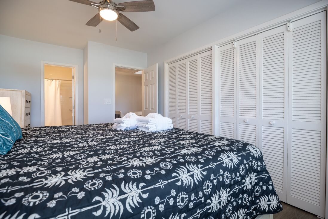 A bedroom with a bed, a ceiling fan, and white closets.