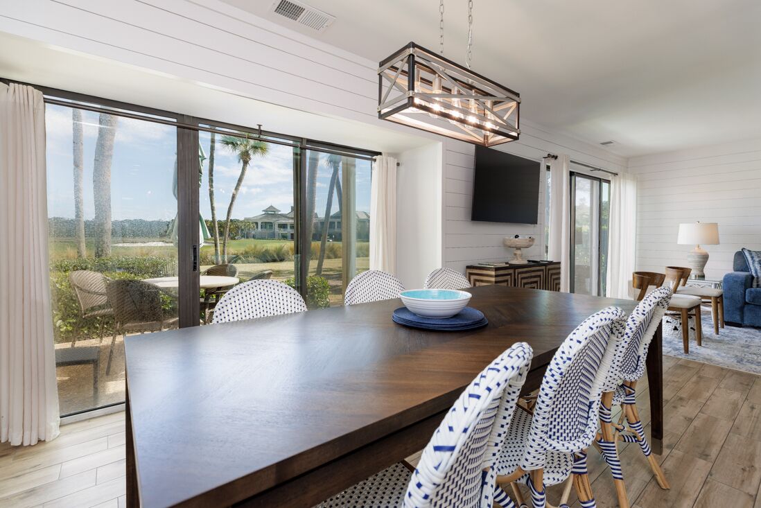 Un espace repas moderne avec une grande table, des chaises en osier et une vue sur l’extérieur.